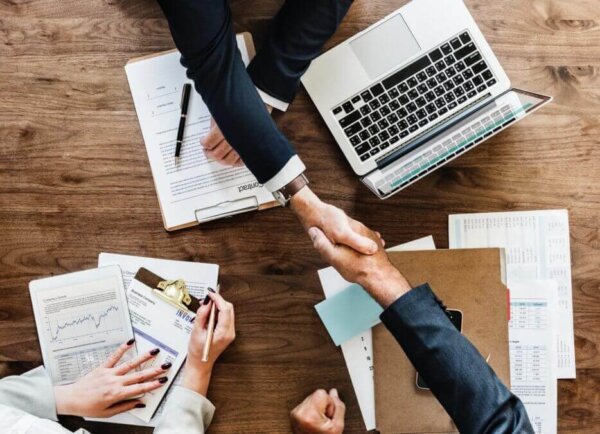 people shaking hands with documents and laptops on the table