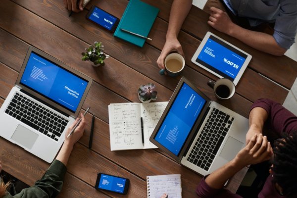 Overhead view photo of people sitting near wooden table on their laptops