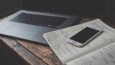 laptop and mobile phone on a desk with notes from research on saas free trial mistakes done by The Good.