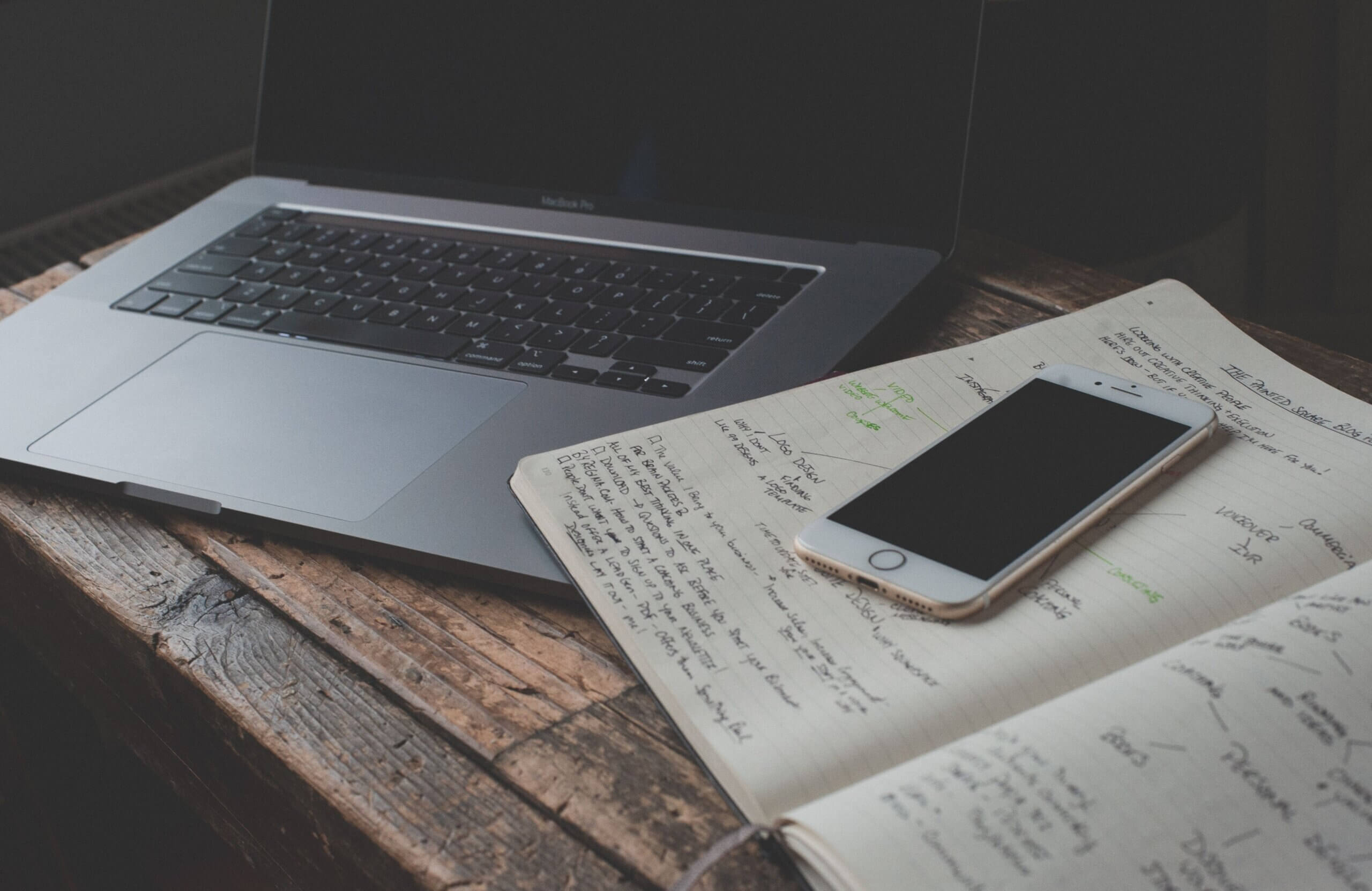 laptop and mobile phone on a desk with notes from research on saas free trial mistakes done by The Good.
